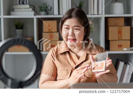 E-commerce entrepreneur demonstrating eyeshadow palette on camera, engaging audience from home office 122717004
