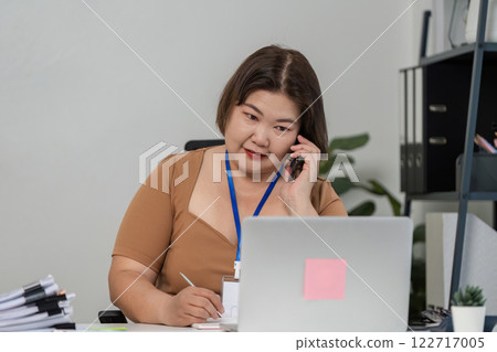Businesswomen communicating on the phone while taking notes in a contemporary office setting Businesswomen communicating on the phone while taking notes in a contemporary office setting 122717005