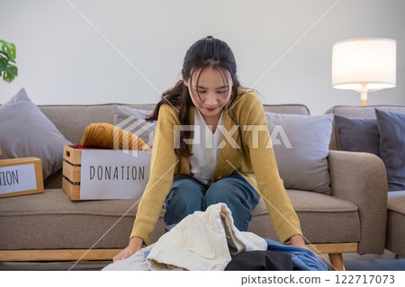 A young woman separates unused clothes and prepares them for donation or recycling in order to reduce air pollution and protect the environment. 122717073