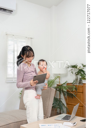 Multitasking mother using tablet while holding her baby, blending technology and parenting at home 122717077