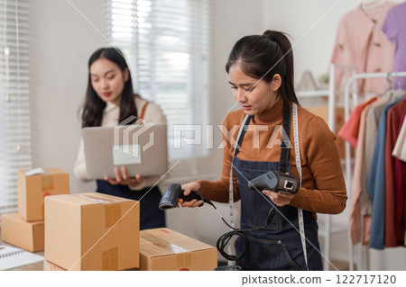 Diligent online sellers managing inventory with barcode scanners and laptop in their organized clothing boutique 122717120