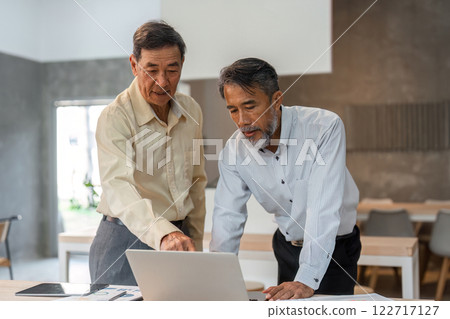 Businessmen collaborating on financial data analysis while pointing at a laptop screen in a modern office Businessmen collaborating on financial data analysis while pointing at a laptop screen in a modern office 122717127