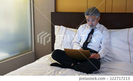 Male business person looking at a laptop computer in bed 122717213