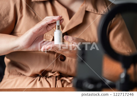 Young woman showcasing skincare serum during a live stream, engaging with viewers as a beauty influencer 122717246
