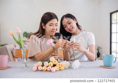 Middle-aged daughter happily arranges flowers with her mother at home Free time activities that are done together as a family 122717405