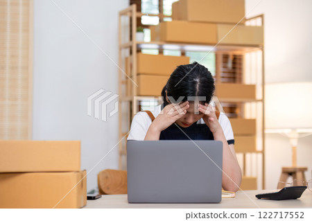 A young female entrepreneur feels stressed about selling products online and preparing to send them to customers. Online selling at home, working from home A young female entrepreneur feels stressed about selling products online and preparing to send them to customers. Online selling at home, working from home 122717552