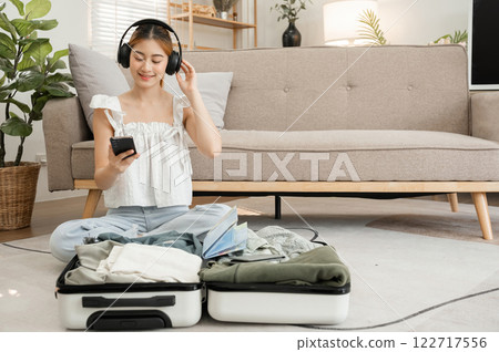 beautiful young woman happy Wear headphones to listen to music while packing your suitcase. beautiful young woman happy Wear headphones to listen to music while packing your suitcase. 122717556