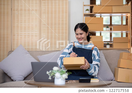 A young Asian entrepreneur sells product online through an online platform and pack product into shipping boxes. A young Asian entrepreneur sells product online through an online platform and pack product into shipping boxes. 122717558
