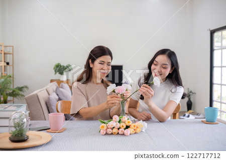 Middle-aged daughter happily arranges flowers with her mother at home Free time activities that are done together as a family 122717712