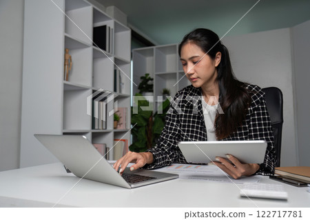 Dedicated Businesswoman Working Late Hours in Modern Office with Laptop and Tablet Dedicated Businesswoman Working Late Hours in Modern Office with Laptop and Tablet 122717781