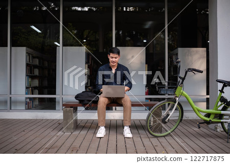 A young Asian businessman rides a bicycle to work. Use a reusable water bottle. Working outside of the office using a laptop The concept of saving energy and reducing pollution to the environment. A young Asian businessman rides a bicycle to work. Use a reusable water bottle. Working outside of the office using a laptop The concept of saving energy and reducing pollution to the environment. 122717875
