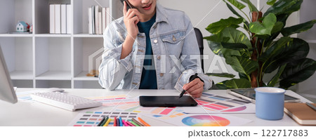 A designer working in graphic design talks in a meeting over tones while choosing colors for work on a computer at his desk at home. 122717883