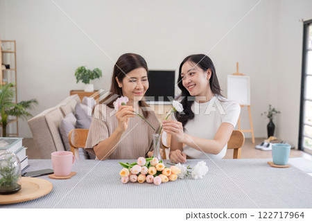 Middle-aged daughter happily arranges flowers with her mother at home Free time activities that are done together as a family 122717964