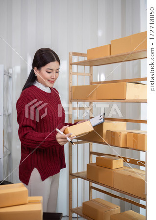 A female Asian online business entrepreneur prepares and packs merchandise into parcel boxes on a table to deliver to customers. 122718050