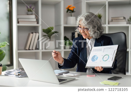 Senior Businesswoman Conducting Online Presentation with Graphs in Modern Office Setting for Virtual Meeting 122718105