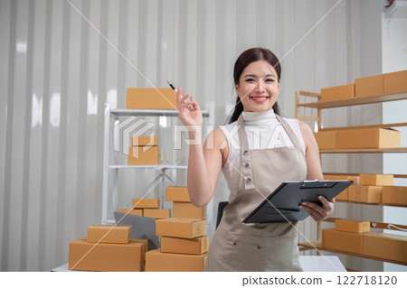 A small SME business owner writes inventory and shipping information on a clipboard in his home office. Small business operators preparing to ship to customers A small SME business owner writes inventory and shipping information on a clipboard in his home office. Small business operators preparing to ship to customers 122718120