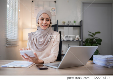 Young Muslim businesswoman holds a meeting over the phone and calculates company finances on her work desk. Young Muslim businesswoman holds a meeting over the phone and calculates company finances on her work desk. 122718122