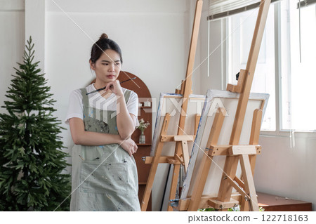 Young Asian female artist is intently painting acrylic paints on canvas in a painting studio. Young Asian female artist is intently painting acrylic paints on canvas in a painting studio. 122718163