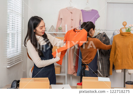 Diverse female e-commerce employees organizing clothing items in retail store. Diverse female e-commerce employees organizing clothing items in retail store. 122718275