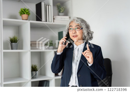 Senior business executive articulating key points on phone in a contemporary office with bookshelves Senior business executive articulating key points on phone in a contemporary office with bookshelves 122718396