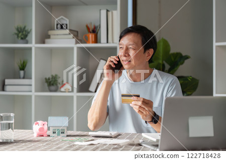 Smiling man using smartphone and credit card for online shopping while talking on the phone 122718428