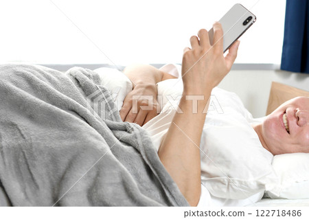 臥室裡拿著智慧型手機的微笑亞洲年輕男子 臥室裡拿著智慧型手機的微笑亞洲年輕男子 122718486