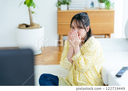 Scared young woman watching TV in the living room Scared young woman watching TV in the living room 122719449