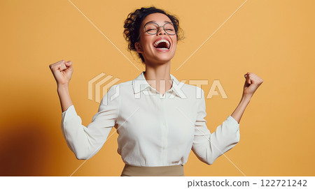 Excited businesswoman celebrating success with raised fists and laughing on yellow background 122721242