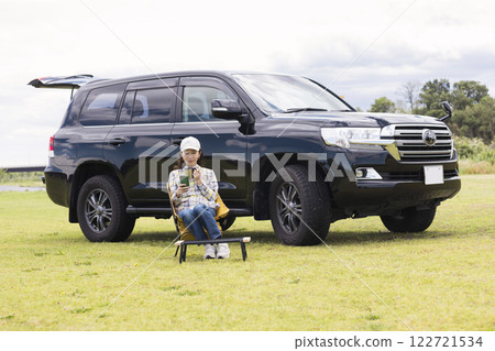 A young woman relaxing while sitting alone on a chair at an auto campsite A young woman relaxing while sitting alone on a chair at an auto campsite 122721534