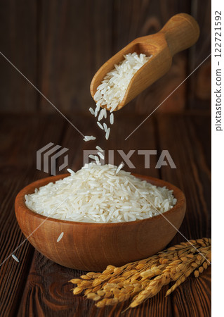 rice falling from scoop in bowl with ears near on wooden background rice falling from scoop in bowl with ears near on wooden background 122721592