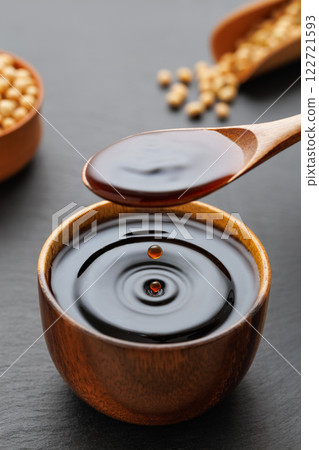 soy sauce pouring from spoon in bowl with splash and drop and dry soybeans on black stone background 122721593