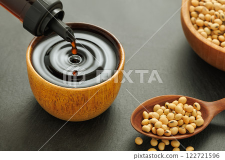 soy sauce pouring from bottle in wooden bowl with splash and drop and dry soybeans on black stone background 122721596