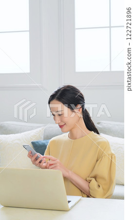 在客廳使用智慧型手機和筆記型電腦的婦女 在客廳使用智慧型手機和筆記型電腦的婦女 122721896