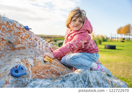 Little girl climbing an artificial climbing wall in a playground, developing strength and coordination Little girl climbing an artificial climbing wall in a playground, developing strength and coordination 122722670