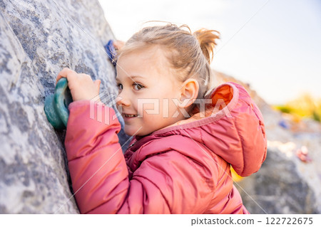 Close up view of little girl climbing an artificial climbing wall in a playground, developing strength and coordination Close up view of little girl climbing an artificial climbing wall in a playground, developing strength and coordination 122722675