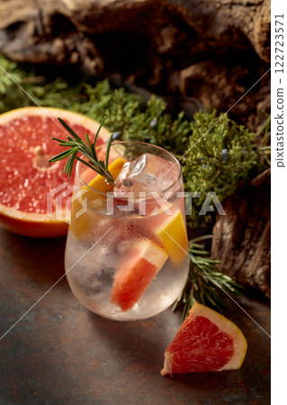 Cocktail: gin and tonic with ice, grapefruit, and rosemary on a rustic background. 122723571