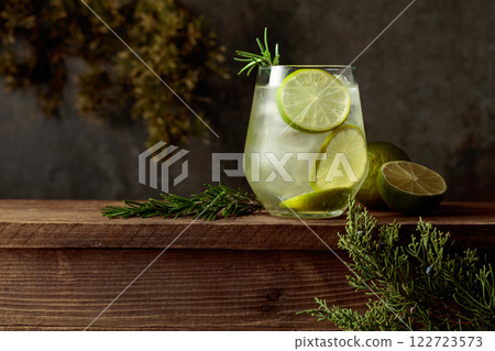 Cocktail: gin and tonic with ice, lime, and rosemary on an old wooden table. Cocktail: gin and tonic with ice, lime, and rosemary on an old wooden table. 122723573