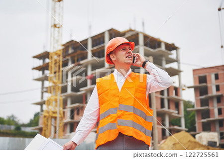 Young architect wearing a protective helmet standing on the mountains building outdoor background Young architect wearing a protective helmet standing on the mountains building outdoor background 122725561