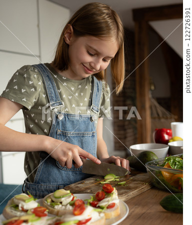 Cute Little Girl Cutting Avocado For Healthy Breakfast, On A Cutting Board In The Kitchen 122726391