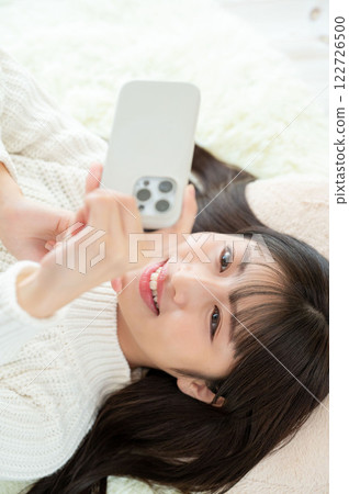 A Japanese woman lying on her back and operating a smartphone 122726500