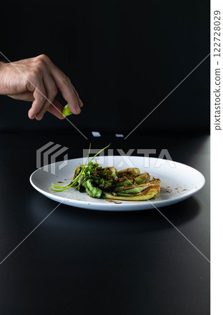 A hand sprinkles lime over freshly cooked bok choy, enhancing flavors in a stylish kitchen. A hand sprinkles lime over freshly cooked bok choy, enhancing flavors in a stylish kitchen. 122728029