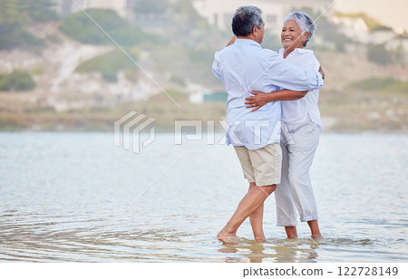Landscape, beach and dance of a senior couple smiling and dancing in the sea or ocean water and hugging at sunset. Happy, smile or bonding of an old man and woman dancing in nature for marriage. 122728149