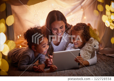 Mother and children live streaming movies on tablet or digital kids app in a tent camping at night and bokeh lights. Care, love mom reading ebook to happy girl or online games with home wifi in dark 122728558