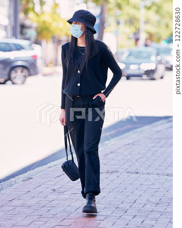 City woman, on a sidewalk, with a mask on her face and walking down the road. Urban fashion, casual walk and covid protection, life in the new normal. Calm beauty, trendy girl walks on the pavement. City woman, on a sidewalk, with a mask on her face and walking down the road. Urban fashion, casual walk and covid protection, life in the new normal. Calm beauty, trendy girl walks on the pavement. 122728630