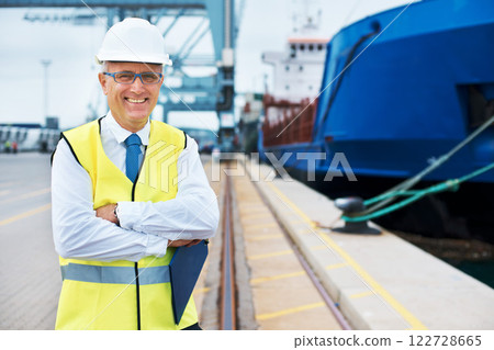 Industrial worker working on a shipping port to export stock, containers and packages. Portrait of logistics, business and industry employee with a crane at a cargo freight warehouse dock. 122728665