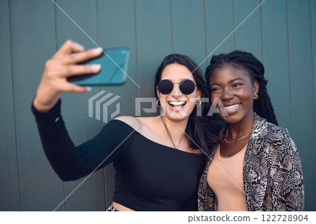 Happy girl friends taking a selfie on phone while traveling around the city on summer vacation. Diversity, love and smiling women taking picture on smartphone to post on social media and the internet Happy girl friends taking a selfie on phone while traveling around the city on summer vacation. Diversity, love and smiling women taking picture on smartphone to post on social media and the internet 122728904