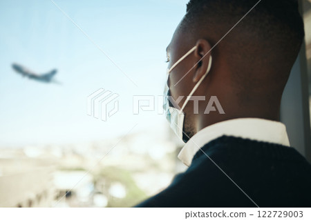 Businessman in an airport for work travel during covid with a mask and plane fly in the background. Entrepreneur, employee or corporate professional watching an airplane while waiting to board flight 122729003