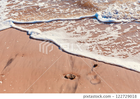 White sea foam contrasting with the dark brown sand in the morning. White sea foam contrasting with the dark brown sand in the morning. 122729018