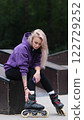 Cute blonde puts on roller skates. She feels free and light while roller skating alone in the city park. Stunning Caucasian woman with a beautiful figure uses roller skates for outdoor sports. 122729252