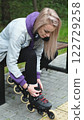 Cute blonde puts on roller skates. She feels free and light while roller skating alone in the city park. Stunning Caucasian woman with a beautiful figure uses roller skates for outdoor sports. 122729258